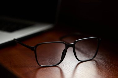 Yakın plan, parlak ahşap bir masada uzanan şık siyah gözlükler profesyonel tasarım ve yaşam tarzı tasvirleri için bulanık arka plan ve doğal sıcak tonlara sahip..