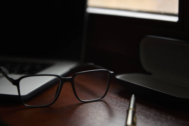 Cilalı bir masanın üzerinde duran siyah gözlük arka planda bilgisayarla profesyonel bir yaşam tarzı ve ofis konsepti yaratıyor..