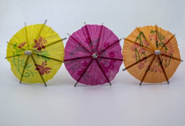 Sarı, pembe ve turuncu renkli üç renkli kokteyl şemsiyesi beyaz arka planda yan yana dizilmiş..