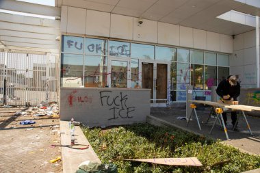 Protestocularla yetkililer arasındaki çatışmanın ertesi sabahı, 15 Haziran 2025 'te Portland, Oregon' daki ICE gözaltı merkezinin ön kapılarını kapatan bir işçi görülüyor..