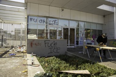 Protestocularla yetkililer arasındaki çatışmanın ertesi sabahı, 15 Haziran 2025 'te Portland, Oregon' daki ICE gözaltı merkezinin ön kapılarını kapatan bir işçi görülüyor..