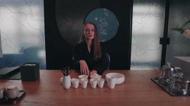 Kamera yavaşça siyah ceketli bir kadını Japon tarzı Asya tarzında bir iç mekanda çay masasında otururken yakalıyor ve elini çenesine koyuyor. Çerçevede geleneksel teaware ve ahşap masa. Yüksek kalite 4k görüntü.