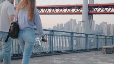 Sunset Man 'de Riverside' da yürüyen çift ve kadın gün batımında nehir kenarında bir gezinti alanında el ele yürüyorlar. Şehir silueti, arka planda köprü. Arka plan, gündelik moda, yüksek kaliteli 4K görüntü.