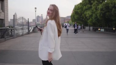 Sosyal medya içeriği yaratan, şehir köprüsünde yürüyen, konuşurken el kol hareketi yapan, milenyum dijital iletişimini ve yaratıcı vlog kültürünü temsil eden bir kadın etkili.