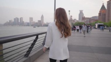 Beyaz spor ceket giyen ve mikrofon taşıyan genç bir kadın gazeteci Shanghai, Çin 'den canlı olarak bildiriyor.