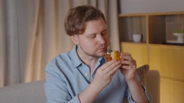 Hamburgeri yerken, yemek pişirmekten zevk alan, gözlerini kapatan ve yavaş çekim sekansında her ısırığın tadını çıkaran genç bir adam, keyifli gastronomik anın altını çiziyor.