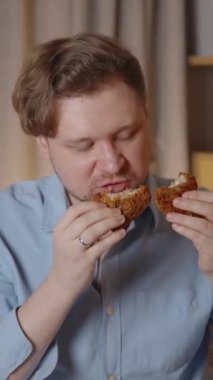 Genç adam, oturma odasındaki kanepede rahat bir şekilde otururken kızarmış tavuğun tadını çıkarıyor. Yavaş çekim zevki sırasında gözlerini kapıyor.