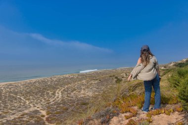 Nazare 'deki Praia do Norte (Kuzey Sahili)' nin vahşi manzarasına hayran olan kız, dev beyaz dalgaları nedeniyle sörf durumu ile ünlüdür.