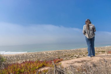 Nazare 'deki Praia do Norte (Kuzey Sahili)' nin vahşi manzarasına hayran olan kız, dev beyaz dalgaları nedeniyle sörf durumu ile ünlüdür.