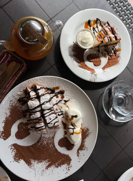 Waffle, dondurma ve üzerine pudra şekeri ve kakao serpiştirilmiş soslu güzel bir tatlı. Bitkisel çaydanlık kompozisyona sıcaklık katar. Sanatsal kakao kalp şekilleri tabakları süslüyor. Yemek için mükemmel bir görüntü. 