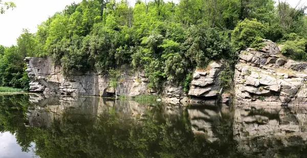 Katmanlı kaya oluşumlarına sahip manzaralı taş uçurumlar yemyeşil ormanlarla çevrili, sakin karanlık suların üzerinde su zambakları ve sazlıklarla kaplı, yaz doğa manzarası, sakin açık hava manzarası, Ukrayna.