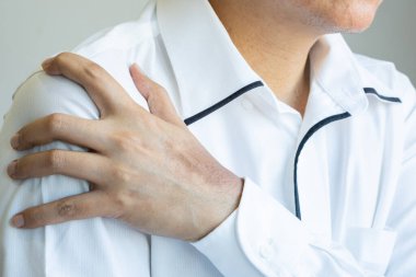 Asyalı bir adam sağ omzunu tutar, lokal ağrı ya da kas dokusunun gerildiğini öne sürer.Kapalı alandaki günlük aktivitelerle ilgili ipuçları verir. Sağlık ve Tıp Konsepti.