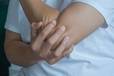 Dirseğini aniden acıtan bir adam. Hafif bir iç aydınlatma ve beyaz bir gömlek tıbbi kaygılarla dolu sakin bir alanı ön plana çıkarıyor. Sağlık ve Tıp Konsepti.