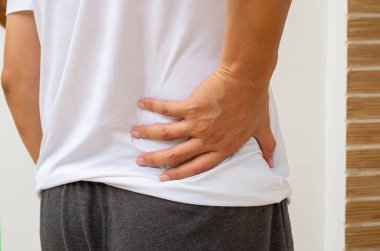 Asyalı bir adam günlük rutininden kaynaklanan bel ağrısı belirtileri gösterir. Kötü duruş, gerginlik veya uzun süreli oturma düzensizliği ya da lokal rahatsızlığa neden olur..