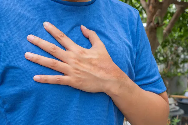 Antrenman sonrası göğüs ağrısı çeken Asyalı bir adam göğsünü endişeyle tutuyor. Jimnastik arka planı. Kalp hastalığı, solunum sorunları ya da kalp riski için uygun. Sağlık ve Tıp Konsepti.