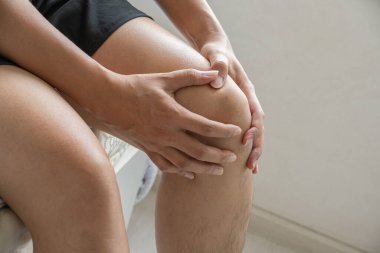 Asyalı bir adam sabah yatak odasında uyandıktan sonra sol dizinde ağrı yapıyor. Eklem iltihabı veya tıbbi sağlık reklamları için eklem ağrısı kavramı.