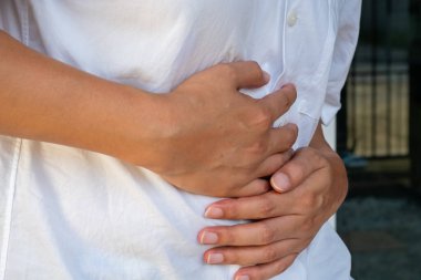 Karın bölgesini nötr bir zemine bastıran bir elin yakın çekimi gastrointestinal rahatsızlığı ve bağırsak ağrısını vurgular. Mide ve bağırsak rahatsızlığı tedavisi için ideal..