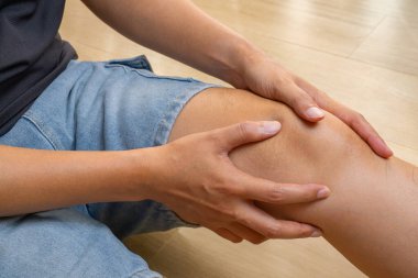 Asyalı adam ahşap zemine oturmuş, diz kapağı zedelenmesi, eklem iltihabı, gut ya da bağ dokusunda zorlama yapıyor. Hedeflenen tıbbi reklamlar için ideal..