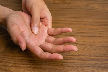 Tekrarlanan iş stresinden kaynaklanan el ağrısının yakın çekimi; bir el, ergonomik stres ve kas iskeleti rahatsızlığını vurgulayarak, diğerinin avucunu ahşap bir masanın üzerine bastırır..
