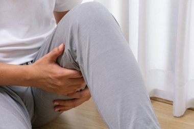 Asyalı bir adam ahşap zeminde oturuyordu. Elinde sabah sakatlığı vardı. Parlak kapalı alanda yumuşak perdelerle egzersiz yaparken kas zorlanması.