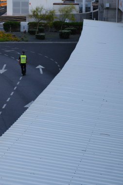 Yalnız, yaşlı, gri saçlı bir liman polisi asfalt boyunca yürüyor..