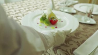 Garsonun eli beyaz tabağı ve organik diyet yemeğini masaya koyar. Lokantada somon yemeği.