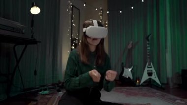 VR kulaklıklı bir kız, giyilebilir VR, ev teknolojisi ve düşük ışıkla bateri çalan neşeli bir kız.