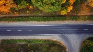 Hava manzaralı insansız hava aracı, güneşli bir sonbahar gününde, kırsal köy yolunun üzerinde, sinematik, canlı, renkli ormanlarla çevrili bir şekilde gidiyor..