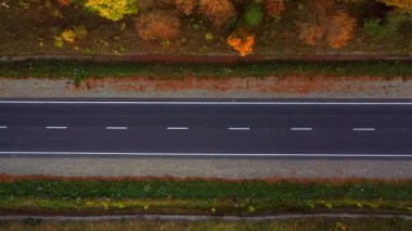 Hava manzaralı insansız hava aracı, güneşli bir sonbahar gününde, kırsal köy yolunun üzerinde, sinematik, canlı, renkli ormanlarla çevrili bir şekilde gidiyor..