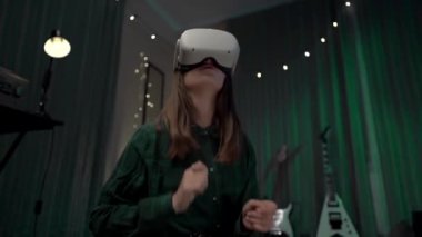 VR kulaklıklı bir kız, giyilebilir VR, ev teknolojisi ve düşük ışıkla bateri çalan neşeli bir kız.