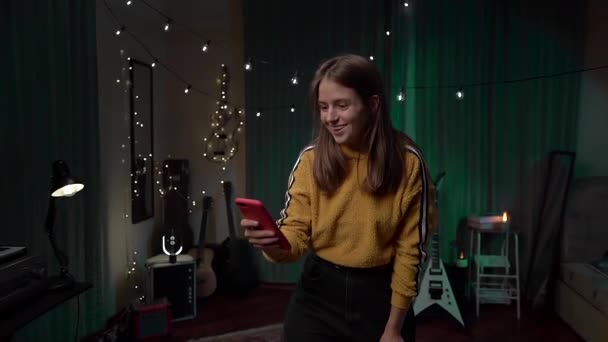 レッドスマートフォンを見て勝利の入札を祝う若いユーフォリック女性 感情の女の子は黄色のセーターで赤い電話でとても幸せ — ストック動画