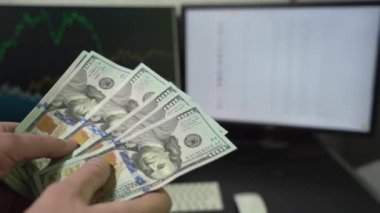 Masaüstünde ticari grafiklerle birlikte Amerikan dolarlarını içeride hesaplayan bir adam. Finans ve Para Ödeme Konsepti.