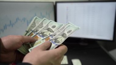 Masaüstünde ticari grafiklerle birlikte Amerikan dolarlarını içeride hesaplayan bir adam. Finans ve zenginlik kavramı. Nakit Yüz Dolar Sayan İşadamı. Finans ve Para Ödeme Konsepti.