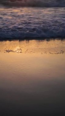 Okyanus dalgalarının üzerinde gün batımı kumlu sahili yıkar. Dikey video. Yüksek kaliteli görüntüler