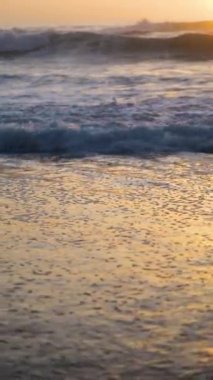Okyanus dalgalarının üzerinde gün batımı kumlu sahili yıkar. Dikey video. Yüksek kaliteli görüntüler