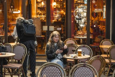 16 Mayıs 2023, Paris, Fransa. Bar ve restoran müşterileri bira içiyor ve cep telefonu kullanıyor. Paris Mahallesi 'nde alışveriş merkezleri ve arabalarla akşam etkinliği.