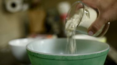 Bir insan elinin, bir konteynırdan karıştırma kabına un dökerkenki yakın çekimi. Bu resim pişirme sürecinin önemli bir adımını yakalar, ev yemeklerini, pişirmeyi ve yemek pişirmeyi sembolize eder..