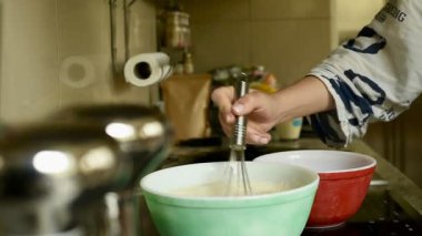 Açık yeşil bir kasede paslanmaz çelik çırpıcıyla hamuru karıştıran bir kadının yakın çekimi. Bu yüksek kaliteli Full HD video çerçevesi ev yemeklerini yakalar. 