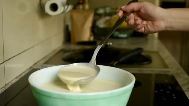 Yüksek kaliteli bir Full HD video çerçevesi. Bir kadının elini ölçmek için metal bir kepçe kullanıyor ve yeşil bir kasedeki ince krep hamurunun tutarlılığını ölçüyor. Ev yapımı kahvaltı için mükemmel..