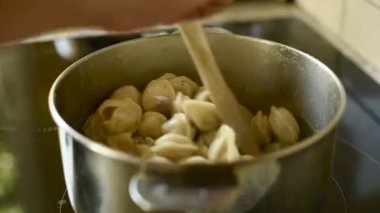 Geleneksel Rus pelmeni 'sini tahta kaşıkla kaynayan bir tencerede karıştıran bir adamın yakın çekimi. Bu çekim yemek pişirme sürecini vurgular ve yapışmalarını engeller..