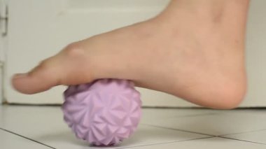 Çıplak ayakla sert, mor bir masaj topuna basan bir kadının yakın çekimi. Bu hareket kan dolaşımını hızlandırıyor ve iç ayak kasları üzerinde çalışıyor..