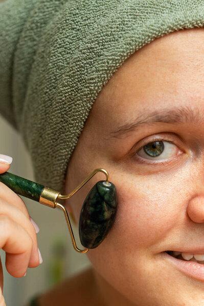 Женщина мягко пользуется каменным массажером на лице, спокойным моментом. Мягкое освещение улучшает спокойную обстановку, идеально подходит для оздоровительных и спа-концепций. Вертикальное фото. 