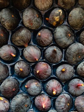 A close-up, vertical shot of ripe, dark organic figs arranged in a cardboard tray at a French bio-market. The image emphasizes autumnal harvest, zero-waste approach, and clean, healthy eating.