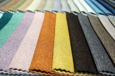 Renkli döşeme kumaşı şeritlerinin yatay çekimini yakın çekimde yapın. Makro bakış açısına göre çeşitli tekstil örnekleri bir kumaş galerisindeki örnek bir kitaba düzgünce yayılmış.