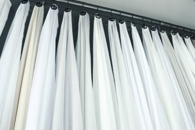 Yatay beyaz ve bej renkli perdeler () kumaş sergi odasında krom bir korkulukta asılı.