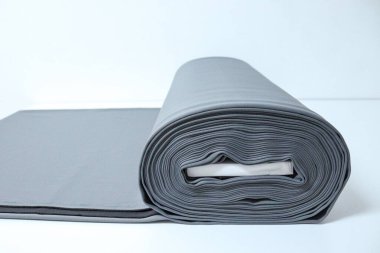Gri perdelerin, beyaz stüdyo masasının üzerindeki kumaş cıvataların göz alıcı yatay görüntüsü. Bir kumaş dükkanındaki kesme yüzeyinde büyük bir rulo sade gri bez duruyor.