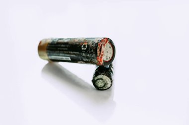 Temiz beyaz bir yüzeye yerleştirilmiş iki ağır aşınmış ve sızdıran AA bataryalarının yakın çekim yatay çekimi. Elektronik atık ve çevre kirliliği kavramı.