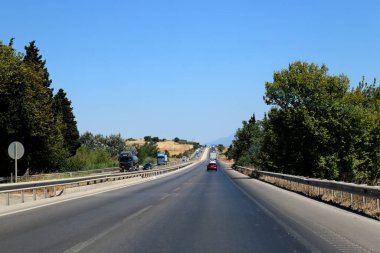 Türkiye 'de düz otoyol, açık mavi gökyüzü altında hafif trafik bulunan kırsal alanlar ve ağaçlar boyunca uzanıyor. Güneşli bir günde iki yönde giden kamyonlar ve arabalar..