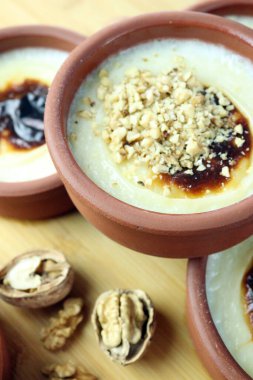 Üzerinde ceviz ezmesi ve karamelize edilmiş yüzey bulunan killi bir kasede pişmiş pirinç sütlü pudinginin yakın çekimi. Geleneksel, sade ve sade sunumlu kremalı tatlı..