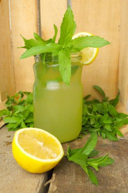 Yaz mojito kokteylini ferahlatıcı cam bir kavanozda taze nane yaprakları ve limonla süslenmiş. Canlı yeşillikle ahşap arka planda kırsal bir sunum.